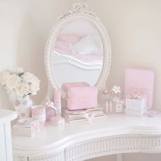 a white vanity topped with a mirror and lots of pink items on top of it