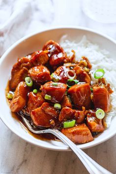 a white bowl filled with meat and rice on top of a table next to a fork