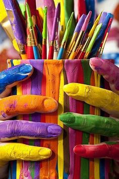 a person holding a cup filled with lots of different colored pens and pencils in it