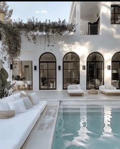 an outdoor swimming pool in front of a large white house with lots of windows and doors