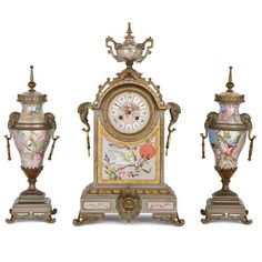 three vases and a clock on display in front of a white background with gold trimming