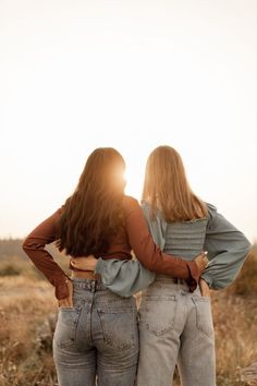 two women standing in the middle of a field with their arms around each other looking at the sky