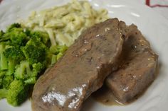 some meat and broccoli on a white plate with gravy over it