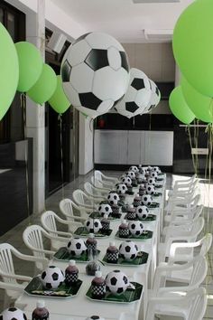 a long table topped with lots of cupcakes covered in soccer balls and balloons