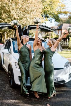 three women in green dresses standing next to a white car with their arms raised up