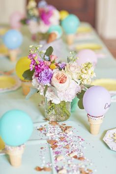 a table with ice cream cones, flowers and balloons in vases on top of it