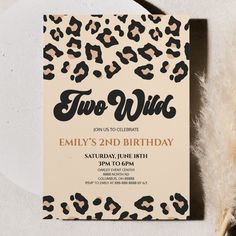 an animal print birthday party card with the word two wild on it, next to a feather