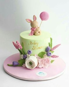 a baby shower cake decorated with flowers and a bunny sitting on it's top