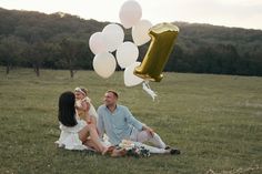 a man and woman sitting on the grass with balloons