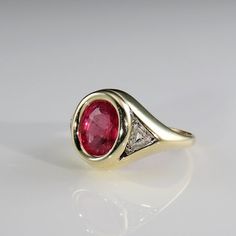 a yellow gold ring with an oval shaped ruby and diamond set in the center, on a white background