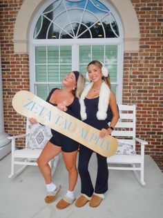 two women standing next to each other holding a skateboard in front of a building