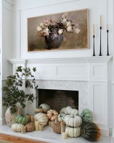 a fireplace decorated with pumpkins and flowers in front of a painting on the wall