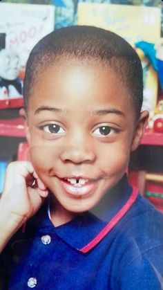 a young boy smiles while talking on his cell phone in front of a book shelf