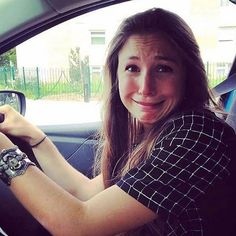 a woman sitting in the driver's seat of a car with her hand on the steering wheel