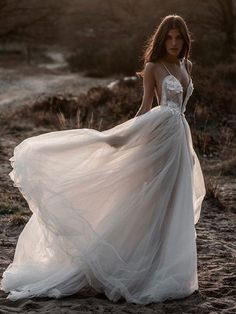 a woman in a white dress is standing on the sand with her hands behind her head