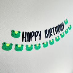 a happy birthday banner with green frogs hanging from it's side on a wall