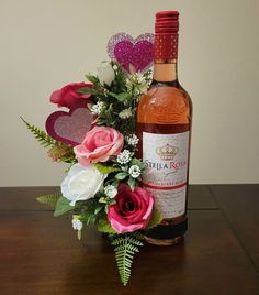 a bottle of wine and some flowers on a table with a corkscrew heart decoration