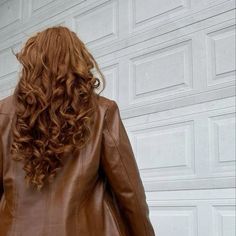 a woman wearing a brown leather jacket standing in front of a garage door with her back to the camera