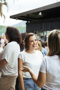 two women talking to each other in front of a group of people at an outdoor event