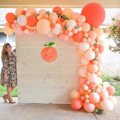 a woman standing in front of an apple themed backdrop with peaches and white balloons