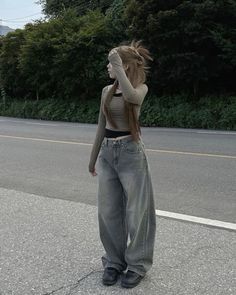 a woman standing on the side of a road with her hair blowing in the wind