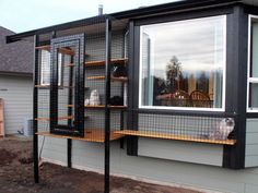 a black and white cat sitting in a cage on the outside of a house next to a window