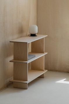 a wooden shelf with a lamp on top of it in front of a beige wall