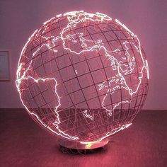 an illuminated globe on a wooden table in front of a pink wall with the world map