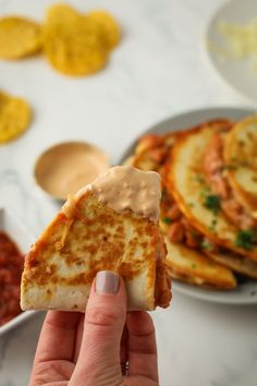 a hand holding up a piece of flat bread with sauce on it and some chips in the background