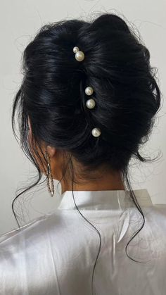 the back of a woman's head with pearls in her hair, wearing a white blouse