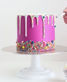 someone is decorating a cake with sprinkles and icing on it