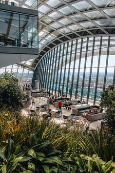 the inside of a building with many plants and people sitting at tables in front of it