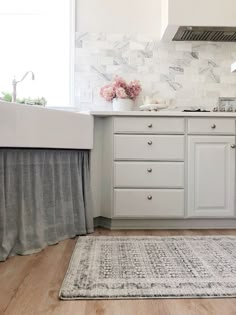 a kitchen with white cabinets and gray curtains on the window sill above the sink