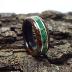 a wooden ring with green and gold inlays sitting on top of a piece of wood