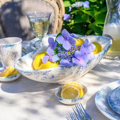 a table set with blue and white dishes, lemons, flowers, and wine glasses