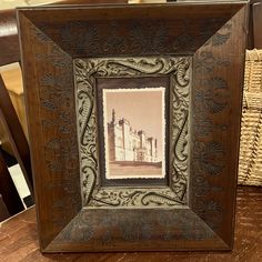 an ornate wooden frame with a picture in it on a table next to wicker baskets