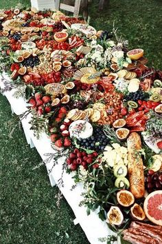 a long table covered in lots of food on top of grass next to a field