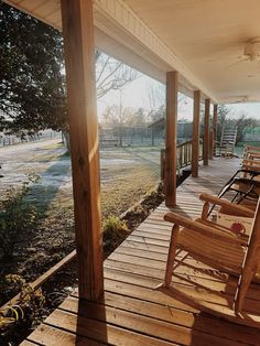 two wooden rocking chairs sitting on a porch next to a tree and grass covered field