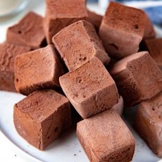 a pile of chocolate fudges on a white plate next to a glass of milk