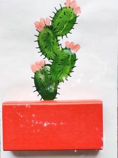 a green cactus with pink flowers sitting on top of a red box