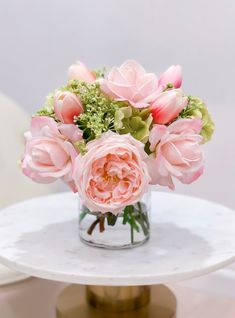 a vase filled with pink flowers sitting on top of a white marble table next to a white chair