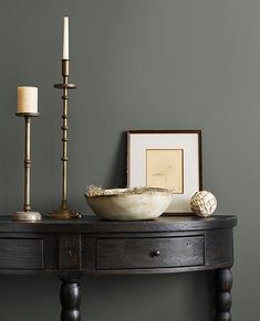 a wooden table with a bowl and two candles on it next to a framed photograph