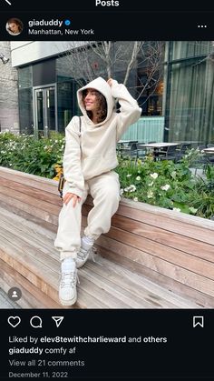 a woman sitting on top of a wooden bench wearing a white sweatshirt and sweatpants