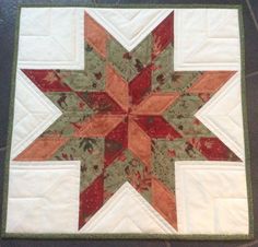 a quilted table topper with an orange and red star on it's center