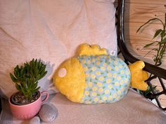 a yellow stuffed fish sitting next to a potted plant