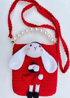 a crocheted red purse with a white rabbit on it's shoulder and pearls hanging from the strap