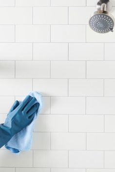 a person in blue gloves and rubber gloves cleaning a white tile wall with a rag