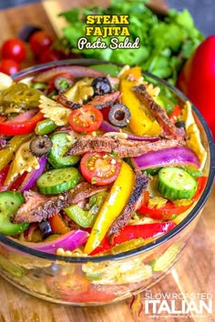 a glass bowl filled with pasta salad on top of a wooden table