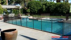 a fenced in swimming pool surrounded by trees and bushes with a large potted plant next to it