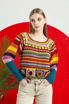 a woman standing in front of a red wall wearing a multicolored knit sweater